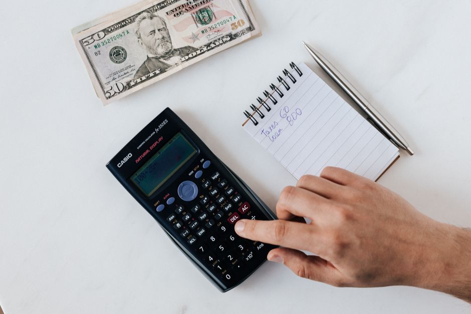 Pessoa calculando fluxo de caixa com calculadora e notas sobre a mesa