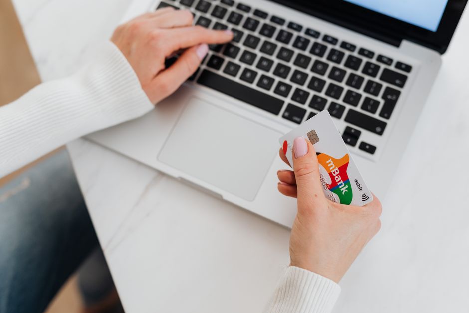 Pessoa segurando cartão de crédito em frente ao notebook para pagamento online