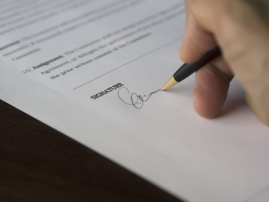 Pessoa assinando um contrato de prestação de serviço em uma mesa de escritório