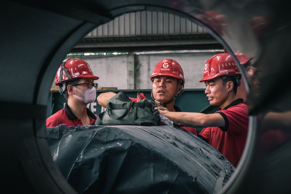 Três trabalhadores de capacete conversando dentro de uma fábrica